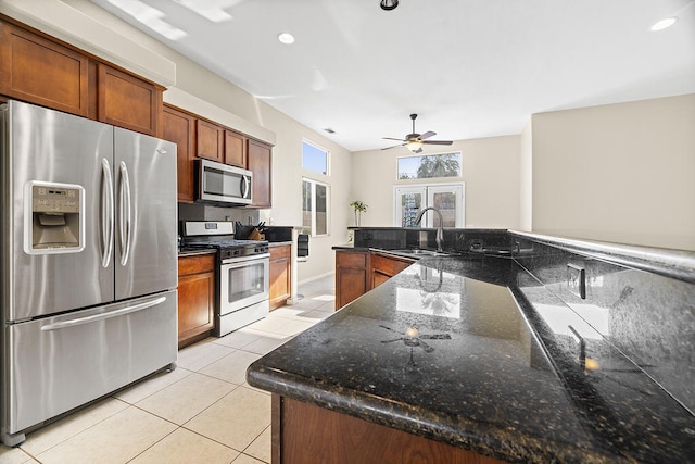 kitchen with light tile patterned floors, ceiling fan, appliances with stainless steel finishes, dark stone counters, and sink