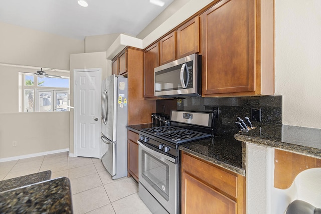 kitchen featuring ceiling fan, stainless steel appliances, tasteful backsplash, light tile patterned flooring, and dark stone countertops