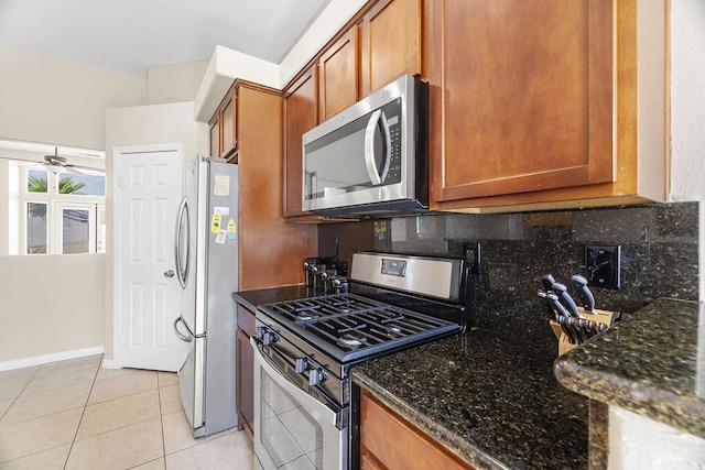 kitchen featuring light tile patterned floors, ceiling fan, stainless steel appliances, backsplash, and dark stone countertops