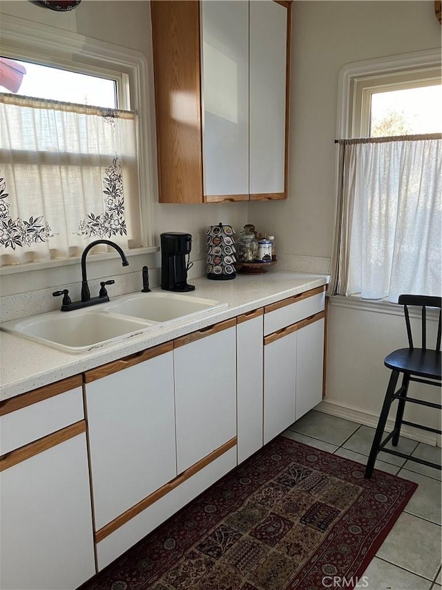 kitchen with white cabinets, light tile patterned floors, a healthy amount of sunlight, and sink