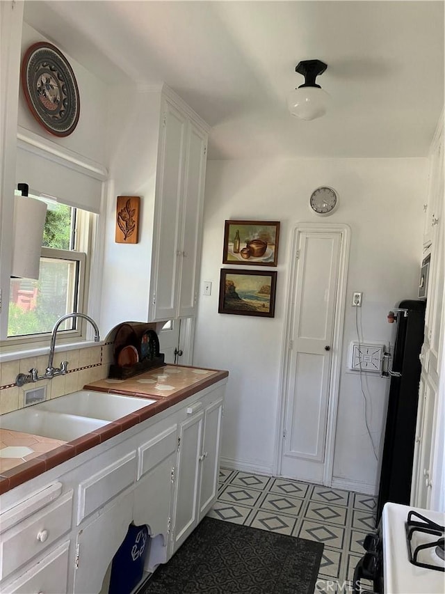 kitchen featuring sink, light tile patterned floors, tile countertops, fridge, and white cabinets