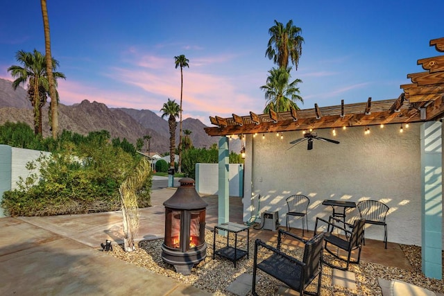 patio terrace at dusk with a mountain view, a pergola, and ceiling fan