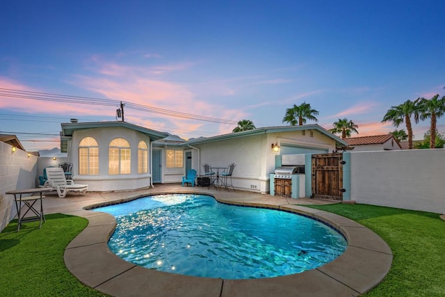 back house at dusk with a fenced in pool, a patio area, a yard, and an outdoor kitchen