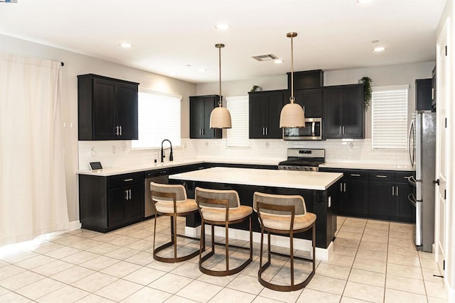 kitchen with appliances with stainless steel finishes, hanging light fixtures, backsplash, a breakfast bar area, and a center island