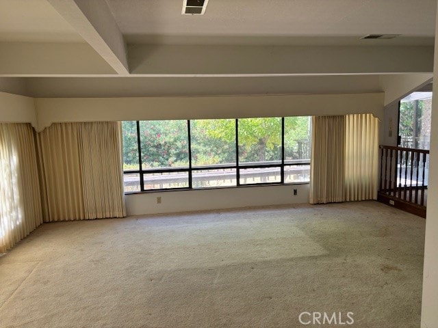 unfurnished room featuring carpet flooring, beam ceiling, and a wealth of natural light