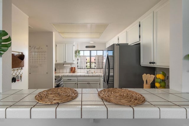 kitchen with white cabinetry, tile countertops, stainless steel fridge, and stove