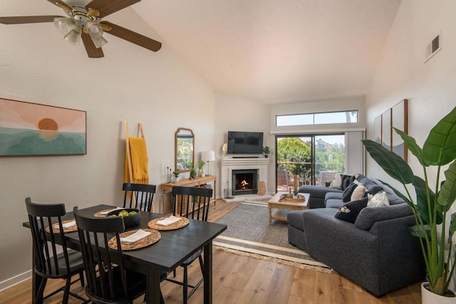 dining space featuring ceiling fan, high vaulted ceiling, light hardwood / wood-style floors, and a brick fireplace