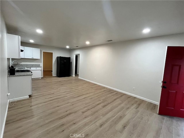 kitchen with dark stone counters, black refrigerator, sink, light hardwood / wood-style flooring, and white cabinetry