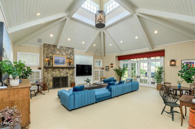 carpeted living room featuring beam ceiling, high vaulted ceiling, a skylight, a stone fireplace, and french doors