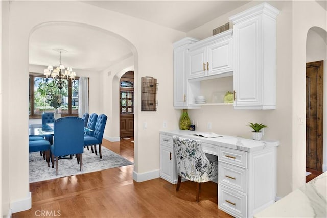 kitchen featuring white cabinets, light hardwood / wood-style floors, an inviting chandelier, and light stone countertops