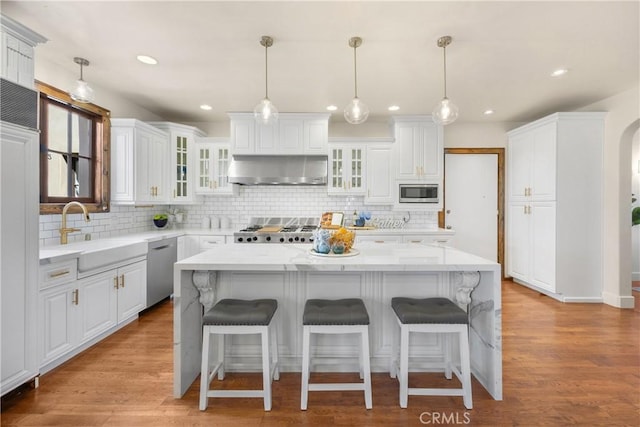 kitchen with pendant lighting, white cabinets, wall chimney exhaust hood, a kitchen island, and stainless steel appliances