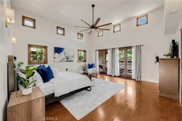 bedroom with a towering ceiling, hardwood / wood-style floors, french doors, access to outside, and ceiling fan