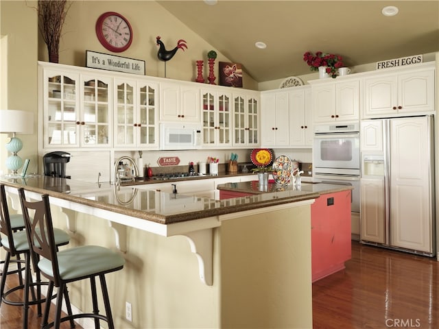 kitchen featuring lofted ceiling, white appliances, a center island with sink, white cabinetry, and a breakfast bar area