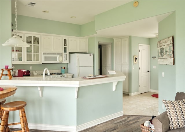 kitchen featuring white cabinetry, white appliances, kitchen peninsula, tile countertops, and light wood-type flooring