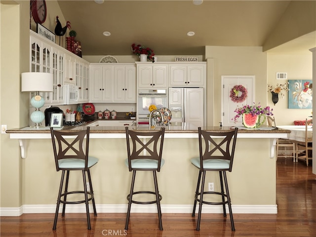 kitchen with a breakfast bar, paneled refrigerator, dark hardwood / wood-style floors, white cabinets, and kitchen peninsula