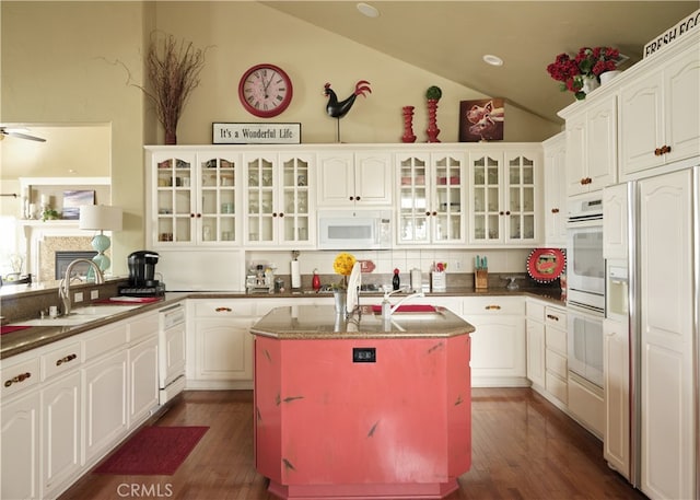 kitchen featuring dark hardwood / wood-style floors, white cabinetry, vaulted ceiling, white appliances, and a center island with sink