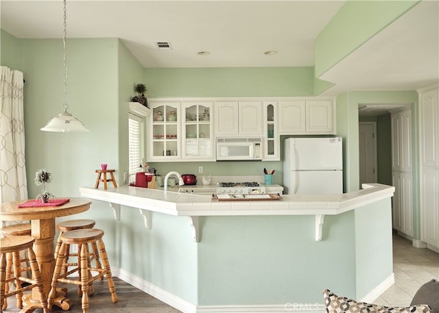 kitchen with a breakfast bar, tile counters, white cabinetry, white appliances, and decorative light fixtures