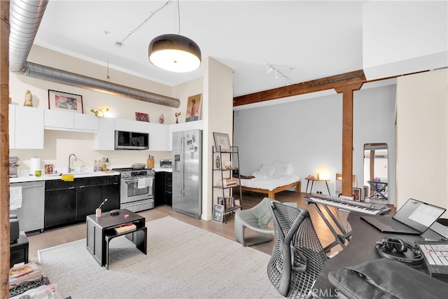 kitchen featuring white cabinetry, rail lighting, light hardwood / wood-style flooring, a towering ceiling, and appliances with stainless steel finishes