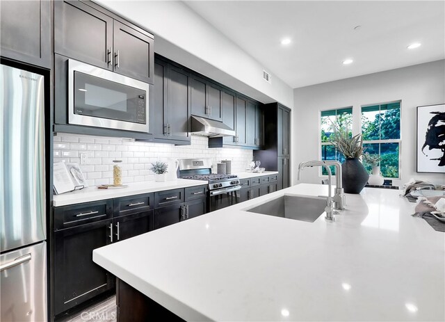 kitchen featuring a kitchen island with sink, appliances with stainless steel finishes, backsplash, and sink