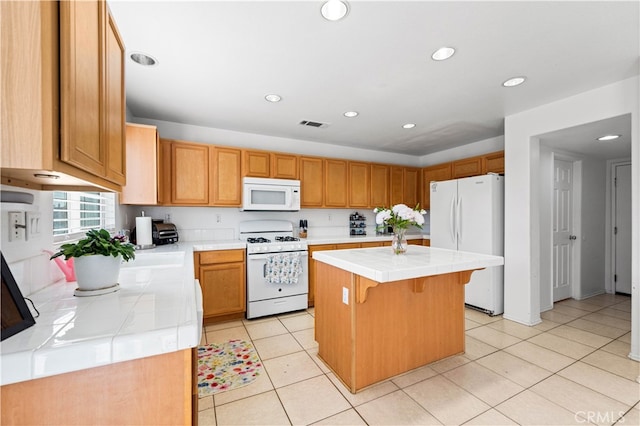 kitchen featuring white appliances, light tile patterned floors, tile countertops, a kitchen bar, and a center island