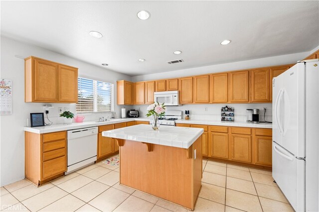 kitchen with light tile patterned floors, white appliances, a kitchen island, tile counters, and a kitchen bar