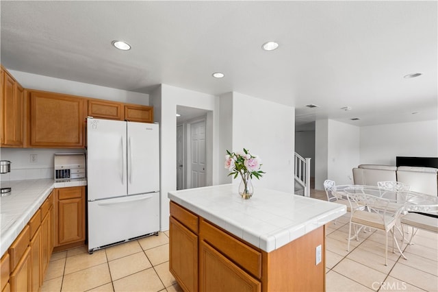 kitchen with tile counters, a kitchen island, light tile patterned floors, and white fridge