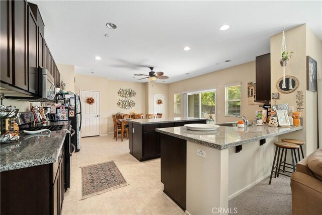 kitchen with sink, ceiling fan, light stone countertops, kitchen peninsula, and a breakfast bar area