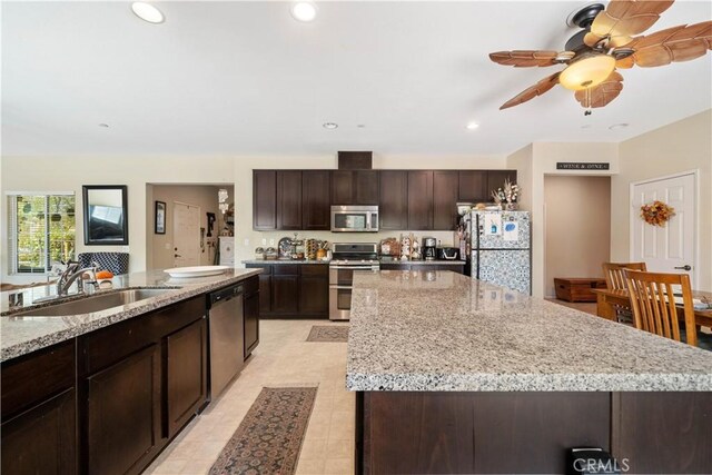 kitchen with dark brown cabinetry, sink, stainless steel appliances, light stone counters, and a spacious island