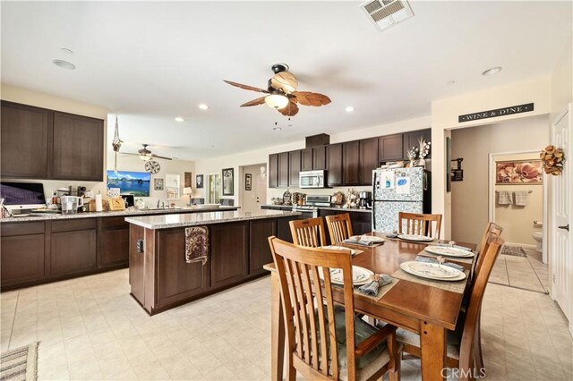 kitchen with appliances with stainless steel finishes, a center island, dark brown cabinets, and ceiling fan