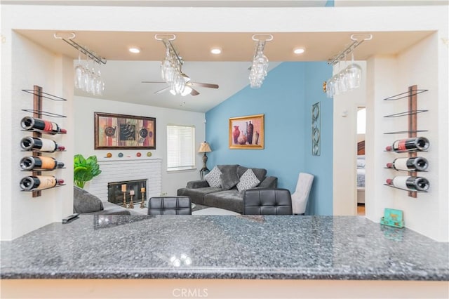 living room with ceiling fan, vaulted ceiling, and a brick fireplace