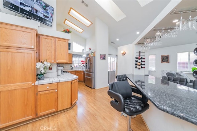 kitchen with high vaulted ceiling, sink, a skylight, stainless steel fridge, and light wood-type flooring