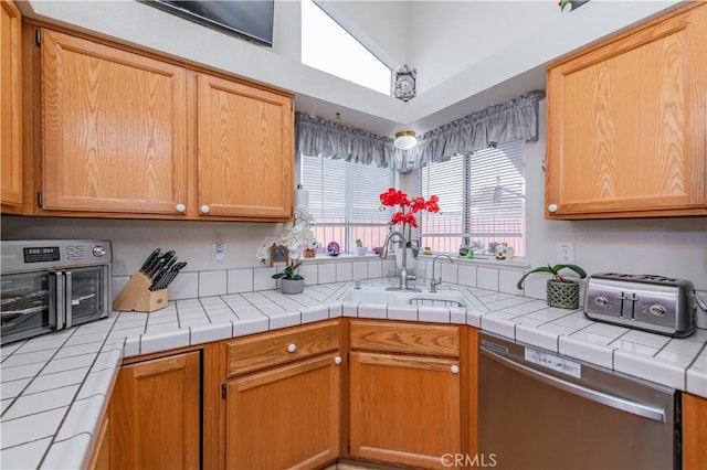 kitchen with tile counters, stainless steel dishwasher, vaulted ceiling, and sink