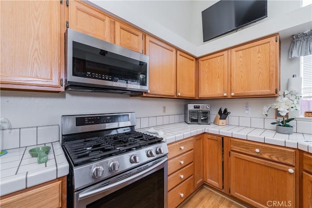 kitchen with appliances with stainless steel finishes, light hardwood / wood-style flooring, and tile counters