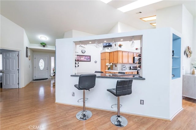 kitchen featuring kitchen peninsula, appliances with stainless steel finishes, light wood-type flooring, high vaulted ceiling, and a breakfast bar area