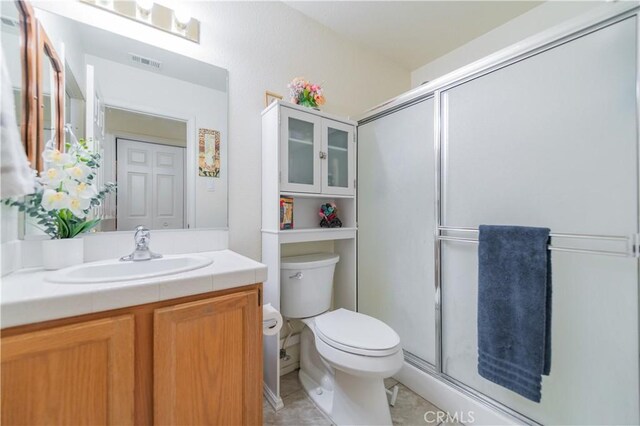 bathroom featuring tile patterned flooring, vanity, a shower with shower door, and toilet