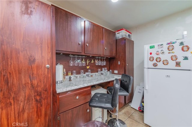 kitchen with white fridge, light tile patterned flooring, light stone countertops, and backsplash