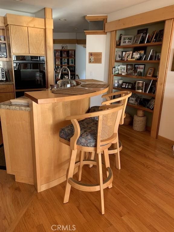 bar with double oven, light wood-type flooring, sink, and light brown cabinetry