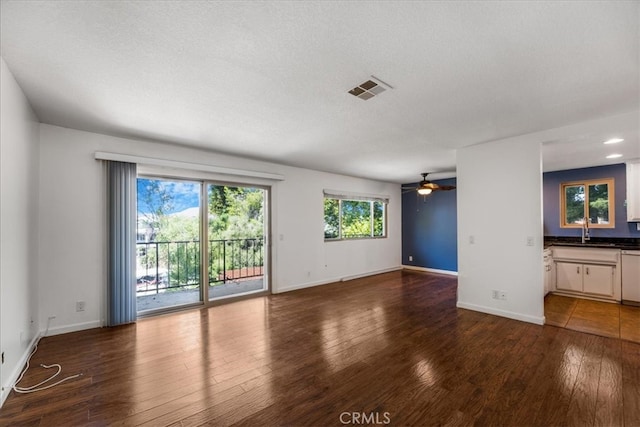 unfurnished living room with a textured ceiling, ceiling fan, dark wood-type flooring, and sink