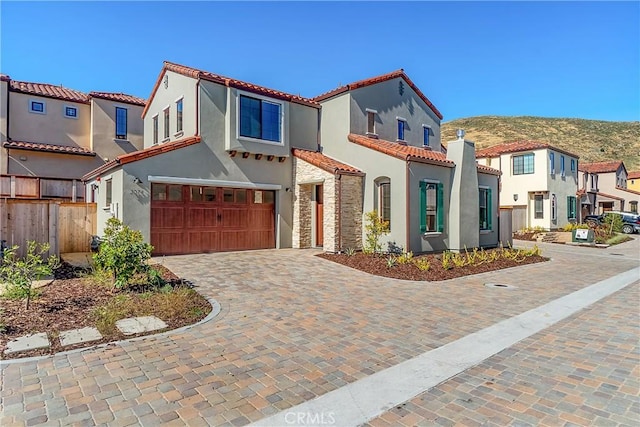 mediterranean / spanish-style home with stucco siding, a tiled roof, decorative driveway, and a garage