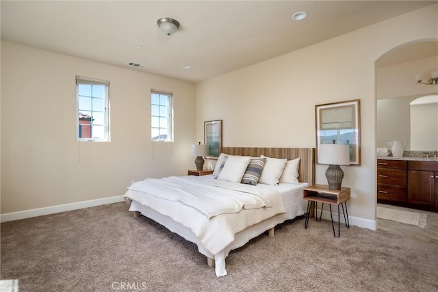 bedroom featuring visible vents, baseboards, light colored carpet, and arched walkways