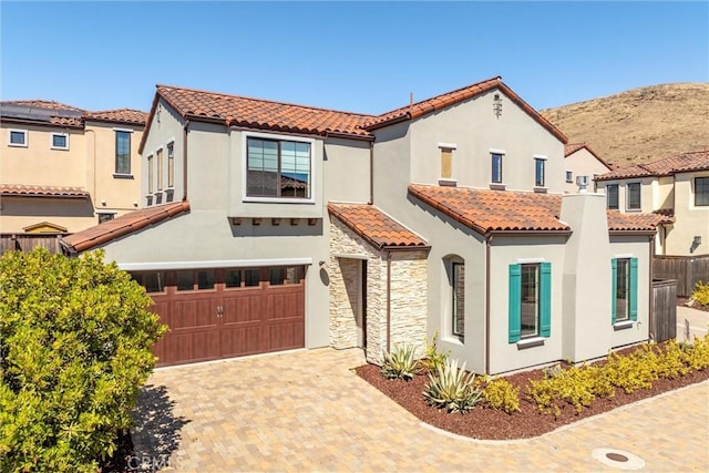 mediterranean / spanish-style home featuring stone siding, stucco siding, a tiled roof, and decorative driveway