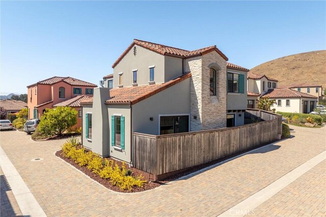 exterior space featuring a tiled roof, a residential view, stone siding, and stucco siding