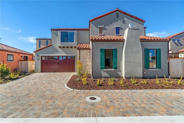 mediterranean / spanish house featuring stucco siding, decorative driveway, a garage, and fence