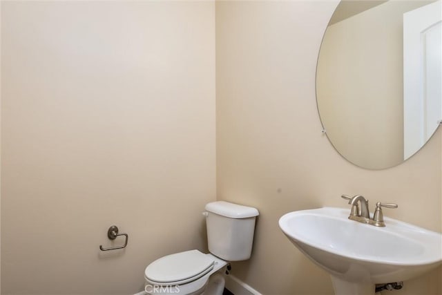 half bathroom with toilet, baseboards, and a sink