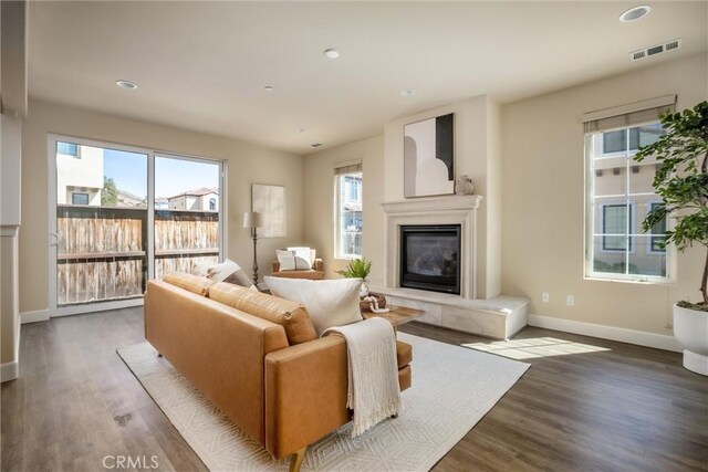 living area featuring a glass covered fireplace, visible vents, baseboards, and wood finished floors