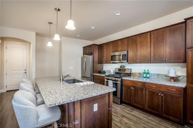 kitchen featuring a breakfast bar area, light stone counters, wood finished floors, a sink, and stainless steel appliances