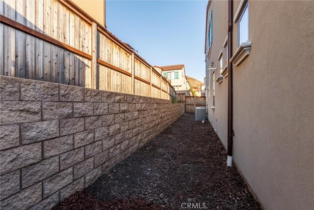 view of side of home featuring stucco siding, central AC, and fence