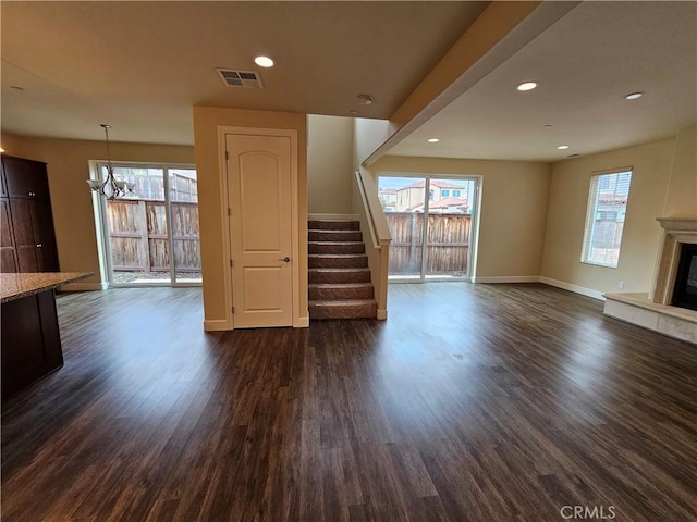 unfurnished living room with stairway, dark wood-style floors, visible vents, plenty of natural light, and a glass covered fireplace