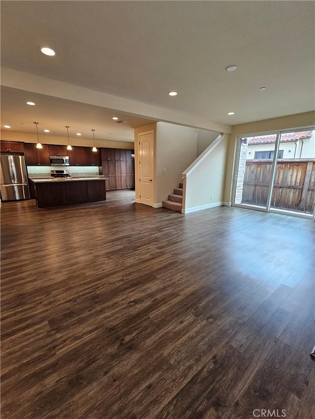 unfurnished living room with recessed lighting, baseboards, dark wood finished floors, and stairs