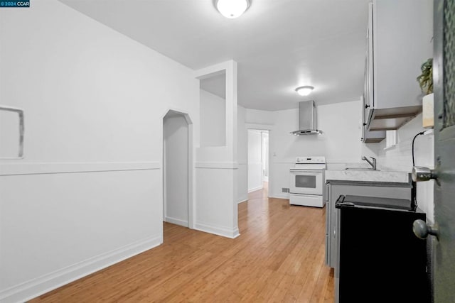 kitchen featuring wall chimney range hood, sink, electric range, and light hardwood / wood-style flooring